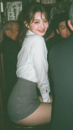 Woman in a white shirt and mini skirt looking over her shoulder indoors