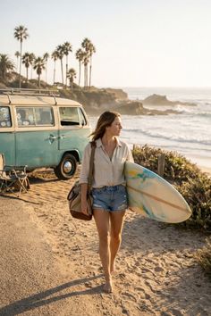 Woman with a surfboard walking barefoot on a sandy path near a beach at golden hour