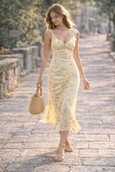 Woman in a yellow floral dress walking outdoors with a straw bag