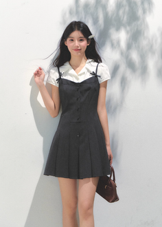 Woman in a pinafore dress and white shirt holding a brown handbag outdoors