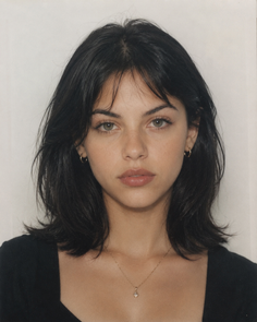 Woman with black medium hair and green eyes wearing a necklace and earrings