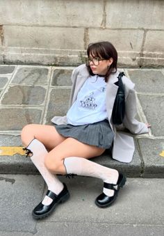 Person in a pleated skirt and knee-high socks sitting on a stone curb
