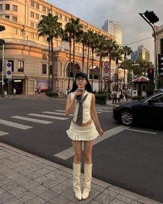 Woman in a white pleated skirt and crop top on a city street with palm trees