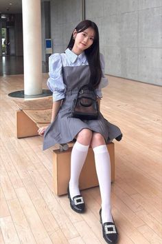 Woman with long hair wearing a gray dress and white knee socks, sitting indoors