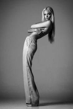 Blonde woman in loose pants posing topless in a studio