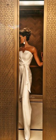 Woman in a white strapless jumpsuit with large earrings in an elevator