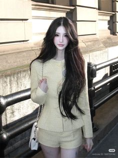 Woman with long dark hair wearing a light yellow tweed suit and shorts outdoors