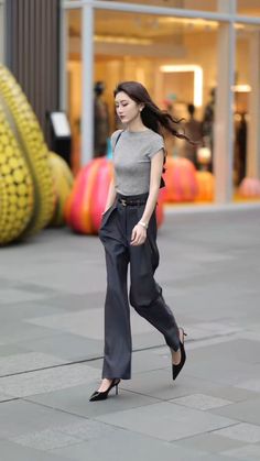 Woman with long hair walking on a street in a grey top and wide leg pants