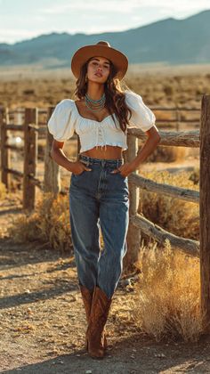 Woman in a cowboy hat, crop top, and jeans standing outdoors at golden hour