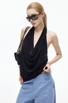 Woman in a black halter top and blue pants with sunglasses and a handbag