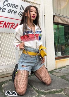 Woman in a crop top, denim shorts, and fishnet stockings posing outdoors