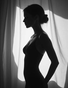 Woman in silhouette against a window with curtains, captured in monochrome