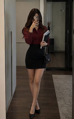 Woman in a red shirt and black skirt taking a mirror selfie indoors
