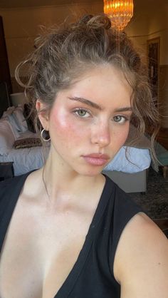 Woman with green eyes and a messy bun wearing a black top indoors