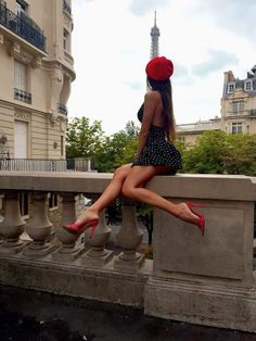 Woman in a red beret and polka dot dress sitting on a stone railing with the Eiffel Tower in the background