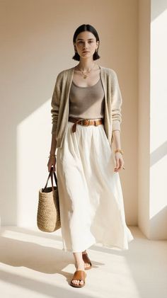 Woman in a cardigan and long skirt holding a straw bag indoors with soft lighting