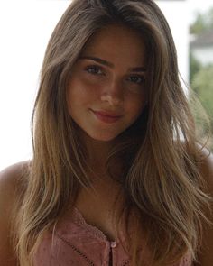 Woman with long hair wearing a pink top with lace trim, soft lighting
