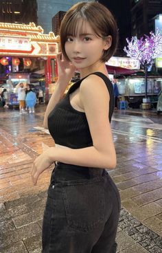 Woman with short hair in a black crop top and jeans on a wet city street at night