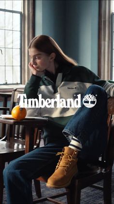 Person in a polo shirt, jeans, and boots sitting by a window with an orange
