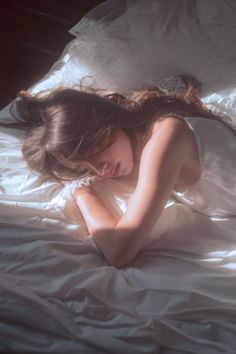 Woman with long hair lying in a white dress on a bed with soft lighting