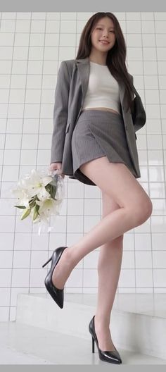 Woman in a gray blazer and mini skirt holding white lilies indoors
