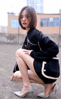 Woman with short hair in a black dress and fur jacket squatting outdoors