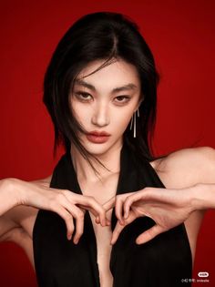 Woman with black hair and long earrings posing against a red background