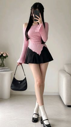 Woman in a pink off-shoulder top and black pleated skirt holding a handbag
