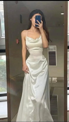 Woman in a white satin dress taking a mirror selfie indoors