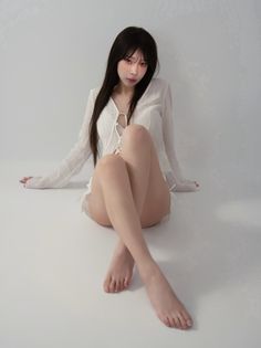 Woman with long dark hair wearing a white top and shorts, sitting on a white floor