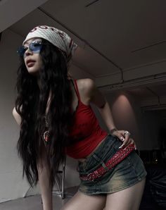Woman with long hair, bandana, and sunglasses in a red tank top and denim skirt