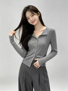 Woman with long dark hair wearing a gray collared cardigan and dark pants