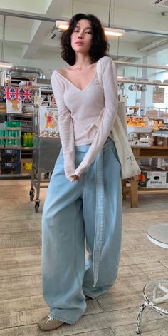 Woman with short curly hair wearing a v-neck top and wide-leg jeans indoors
