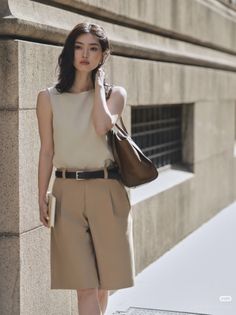 Woman in a sleeveless top and beige shorts with a brown bag outdoors