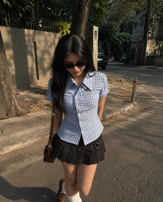 Woman in a plaid shirt and pleated skirt walking on a sunny street