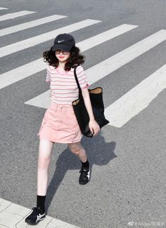 Woman in a pink striped shirt and skirt crossing a street