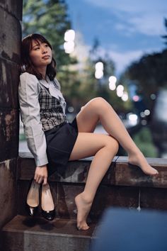 Woman in a school uniform sitting barefoot on a stone ledge at night
