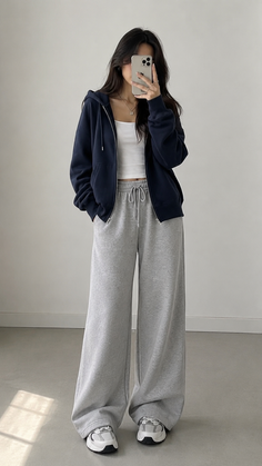 Woman in a navy hoodie and grey sweatpants taking a mirror selfie