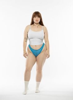 Woman in a white tank top and blue underwear standing against a white background