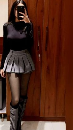 Woman in a black top and pleated skirt taking a mirror selfie