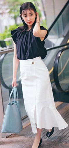 Woman in a black top and white skirt holding a blue handbag outdoors