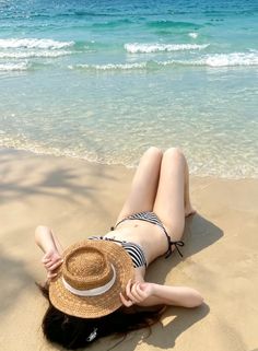 Person in a striped bikini and straw hat lying on a sandy beach