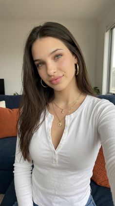 Woman with long hair and gold jewelry wearing a white button-up shirt indoors