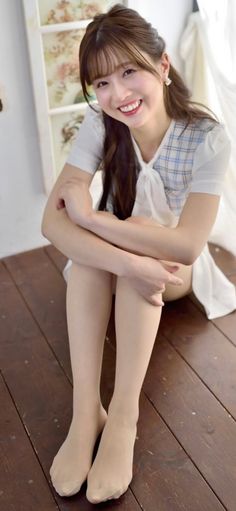 Woman with long hair wearing a plaid dress and white top, sitting on a wooden floor