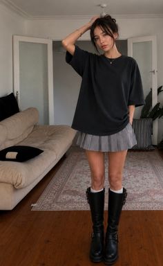Woman in a gray pleated skirt and black boots posing indoors
