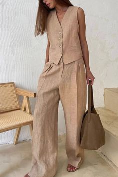 Woman in a beige linen vest and wide leg pants holding a brown bag indoors