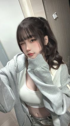 Woman in a gray hoodie and white crop top winking indoors