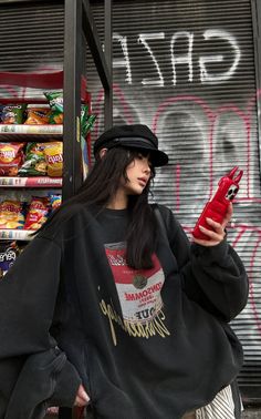 Woman in a black hat and oversized sweatshirt holding a red phone case on a street