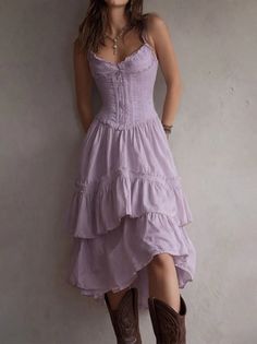 Woman in a purple corset dress and cowboy boots leaning against a wall