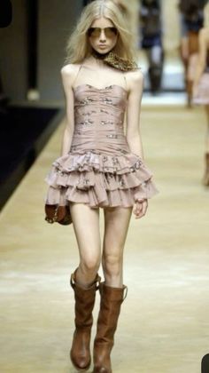 Blonde model in a mini dress, sunglasses, and brown boots on a runway